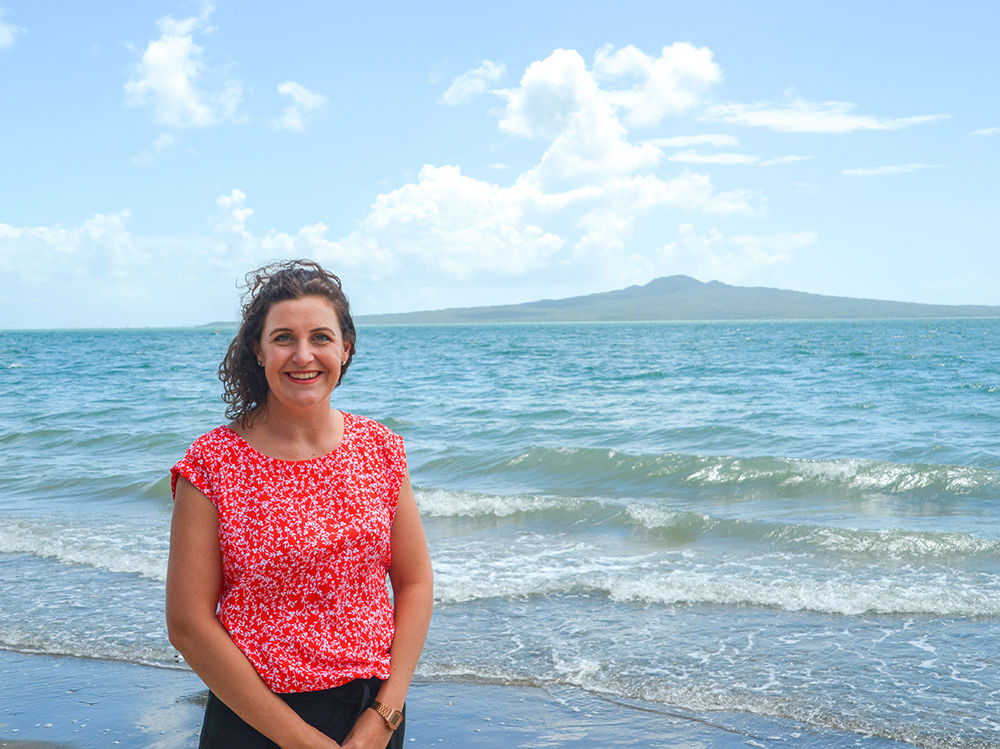 Alisha from MoaTours on the beach at Mission Bay, Rangitoto Island in the background